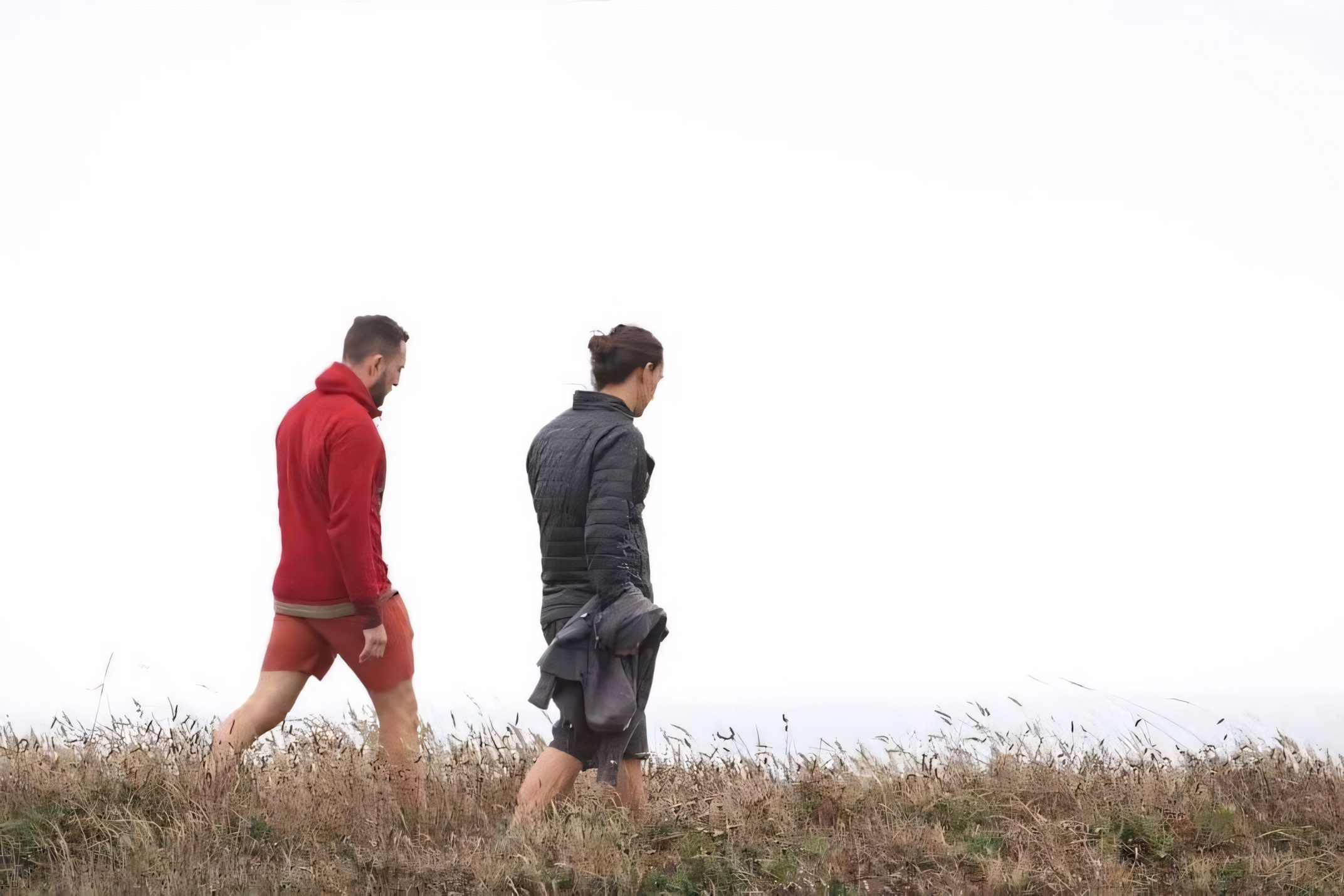 Two people walking together through coastal grass on an overcast morning